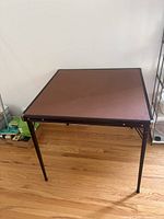 Brown vinyl-top folding card table on hardwood floor