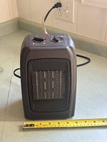Front view of black portable electric space heater with measuring tape showing width ~6 inches
