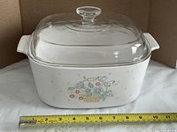 Front view of casserole with lid showing floral basket pattern and measuring tape for scale