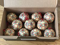 Open box showing 11 floral cream ornaments with red cords