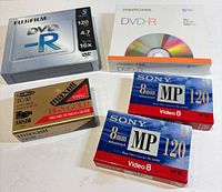 All sealed media packages displayed: Fujifilm DVD-R 5-pack, Memorex DVD-R 5-pack, two Sony 8 mm cassettes, Maxell TC-30 VHS-C