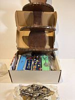 Box holding multiple cased souvenir spoons and disassembled wooden spoon rack, loose spoon pile in foreground