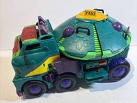 Left side and rear view of teal TMNT taxi vehicle with turtle-shell dome and purple wheels