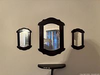 Three dark wood mirrors and matching demi-lune shelf mounted on wall