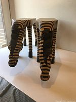 Front three-quarter view of both carved zebra tables showing striped finish and leg design