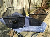 Both black metal mesh bicycle baskets side by side on mat outdoors