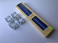 Four glass tealight holders with candles alongside sealed box of blue taper candles