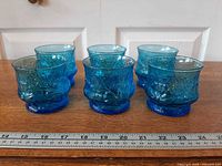 Front view of six blue Rain Flower tumblers on ruler