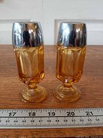 Both amber glass shakers with lids, front view with ruler for scale