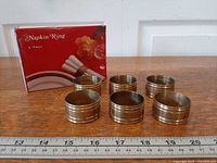 Six brass napkin rings with box and ruler for scale