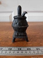 Front view of miniature cast iron pot belly stove beside ruler