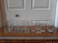 Full set of thirteen clear glass tumblers lined up with ruler for scale