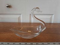 Side view of clear glass swan dish on wood surface showing overall form