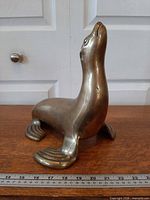Full left side view of brass sea lion on wood surface with ruler for scale