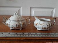 Covered sugar bowl and creamer side by side showing size against ruler