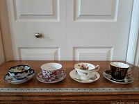 Four teacup and saucer sets on table with ruler for scale
