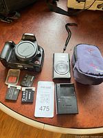 All items in lot laid out: EOS body, PowerShot ELPH camera, batteries, charger, SD card, pouch