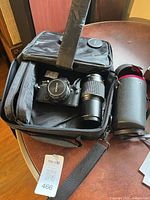 Camera bag opened showing camera, attached lens, zoom lens, and strap tag