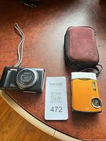 Black Olympus camera, orange Olympus camera, Lowepro case on tabletop