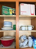 Cabinet shelves with boxed glassware, Gibson dish set, mugs, mixing bowls and packaged items
