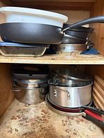 Cabinet shelf showing assorted nonstick and stainless cookware stacked