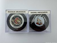 Front view of both signed pucks in cases showing player name labels and signatures