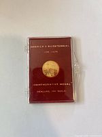 Front view of medal in plastic case showing text America’s Bicentennial 1776-1976 Commemorative Medal Genuine 10K Gold