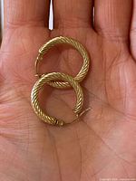 Pair of twisted 10K gold hoop earrings shown on hand for scale