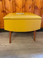 Front view of yellow vinyl storage ottoman on tapered wooden legs