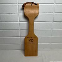 Front view of wooden grill scraper showing shape, handle and leather loop