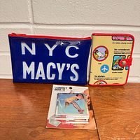 All three items side by side: blue Macy’s pouch, Transversion passport holder, packaged compact mirror