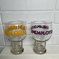 Front view of both novelty beer goblets showing printed slogans