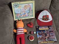 Group shot of all items showing puzzle box, book, hat, plush, yo-yo, heart keychain, bouncy balls
