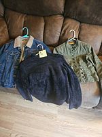 Blue jean jacket, green jacket and black sweater displayed on couch