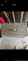 Closed olive drab steel trunk marked BEACON TRUNK
