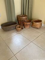 Group of five baskets and two wooden spools arranged on floor
