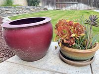 Large burgundy planter and small green gradient planter with saucer on patio