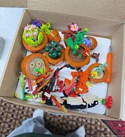 Top view of box showing multiple orange potted LEGO flower builds and loose parts