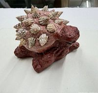 Front view of red clay turtle with seashell-covered shell