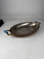 Full view of copper oval pan showing overall shape, interior lining, and both brass handles