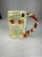 Front view of ceramic mummy mug showing eyes, spider detail, pumpkin accent