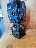 Frontal view of carved wooden Garuda statue showing wings and human figure