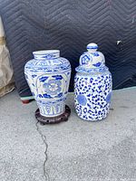 Full view of both blue-white porcelain ginger jars, one on wooden base, showing patterns and shape