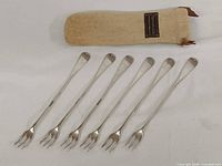 Six sterling silver cocktail forks and flannel pouch displayed on white background