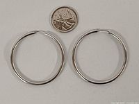 Pair of sterling silver hoop earrings beside coin for scale