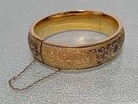 Full view of hinged bangle showing exterior etching and safety chain