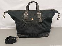 Front view of Coach black jacquard duffle showing logo plaque, handles, detachable strap beside