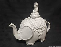 Left-side view of white ceramic elephant teapot with seated figure lid