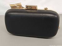 Front view of black leather clutch showing gold clasp and logo