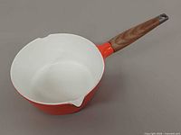 Top angle view of orange enamel saucepan showing white interior and wood handle
